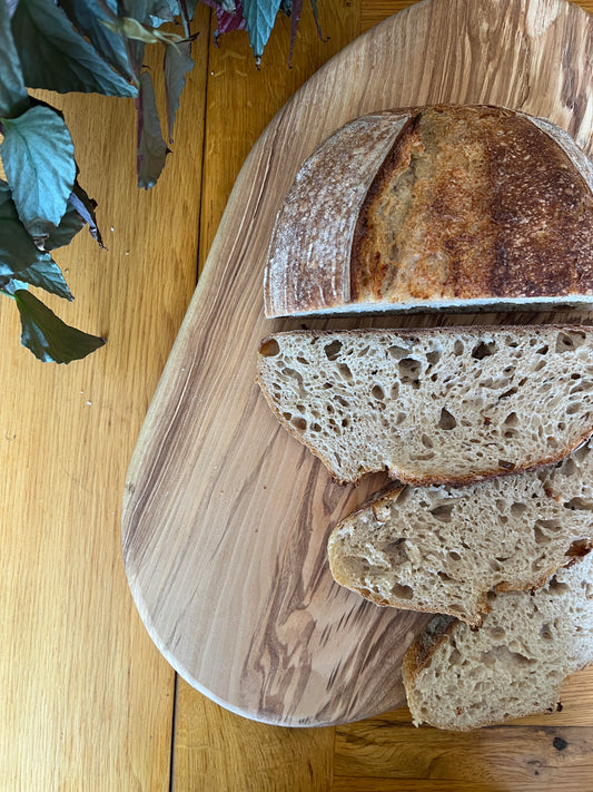 Sliced loaf of bread on a wooden cutting board with a plant in the background